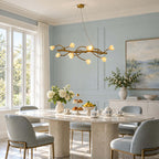A Clérachic blossom-branch chandelier lit above a stone dining table with grey-blue chairs, in a room with pale blue panelled walls.
