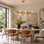 Lit Clérachic blossom chandelier over a round stone table with tan and cream chairs, by tall black-framed glass doors.