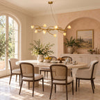 Clérachic magnolia-bloom chandelier hung above a round dining table with cane-backed chairs, in a peach room with arched windows.