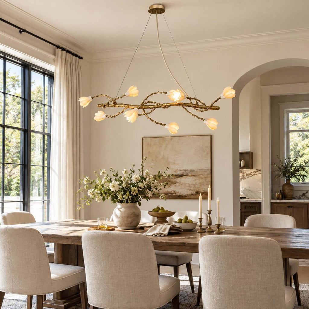 Wide view of this Clérachic gold vine chandelier above a long timber table with cream chairs, with a painting on the wall behind.