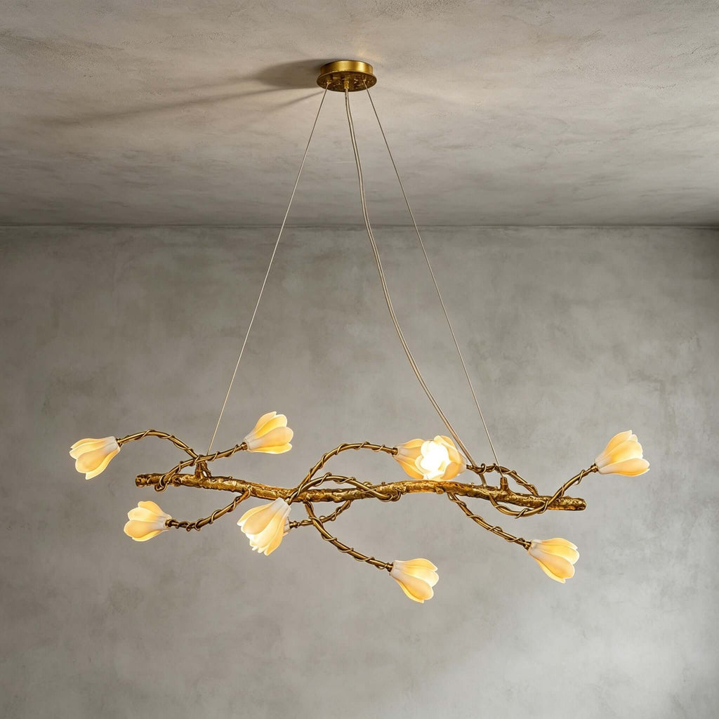 Lit Clérachic magnolia chandelier hung from a gold canopy on fine wires, against a soft grey plaster wall.