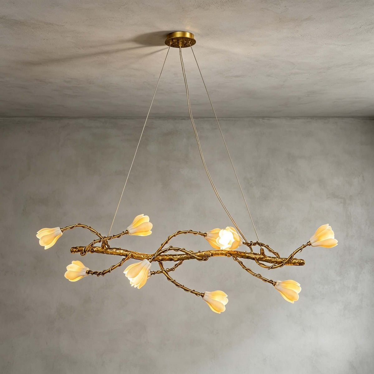 Lit Clérachic magnolia chandelier hung from a gold canopy on fine wires, against a soft grey plaster wall.