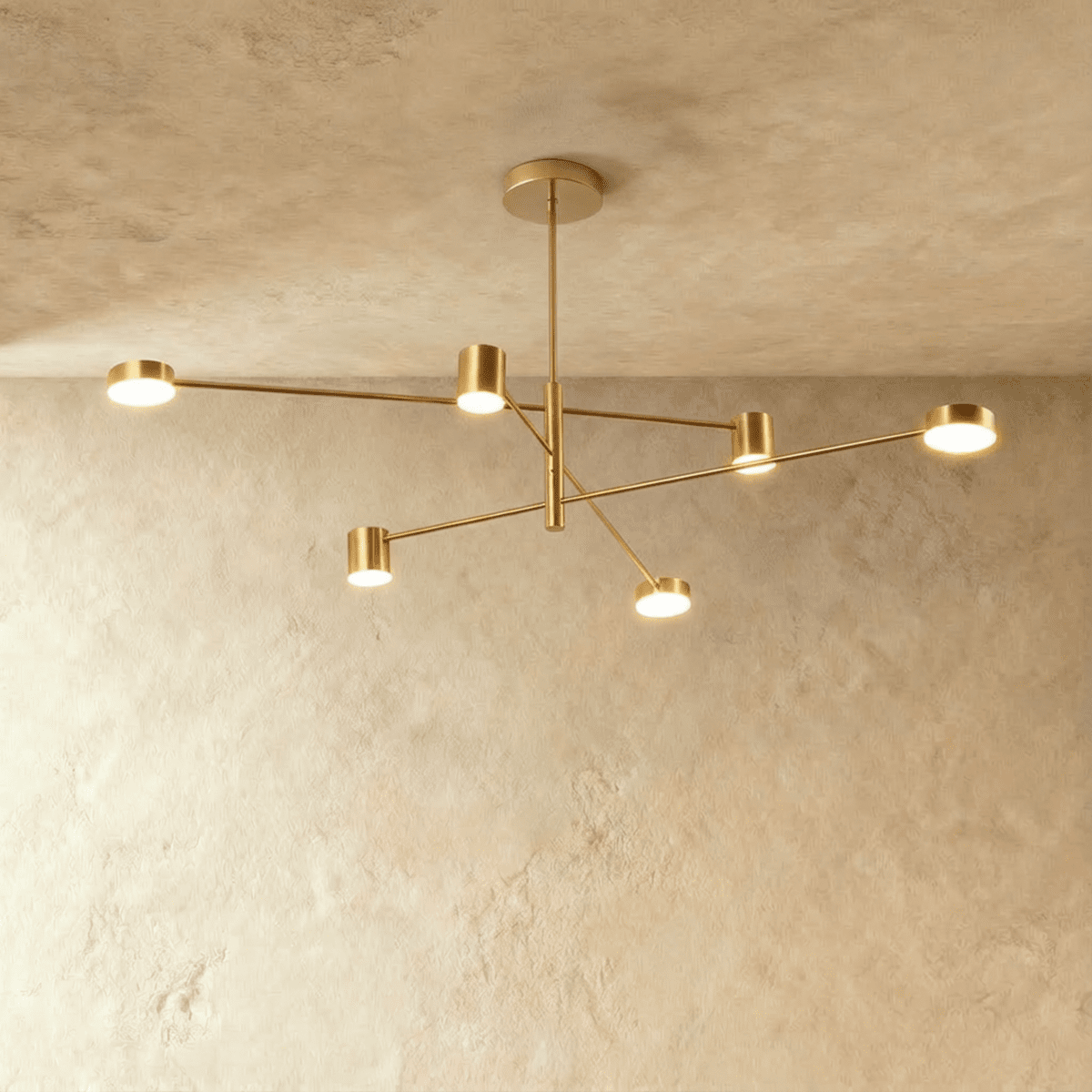 Clérachic six-head gold chandelier with slender arms and cylindrical lights, hung from a round canopy against a pale limewashed wall.