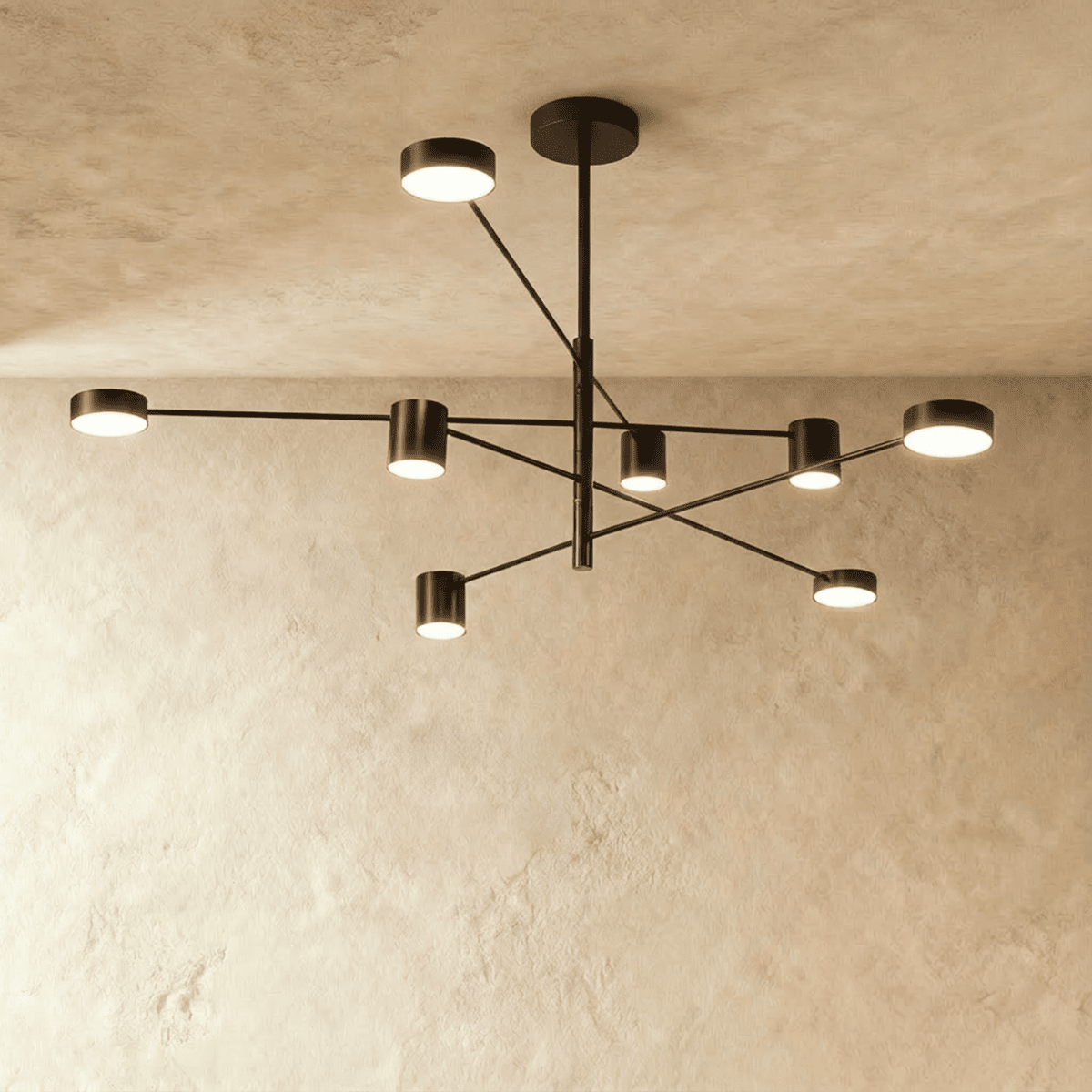 Clérachic eight-head chandelier in dark bronze-black, with slender arms and cylindrical lights, against a pale limewashed wall.