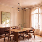 Clérachic black eight-head chandelier with slender arms hung above a wooden dining table in a bright panelled room with tall windows.