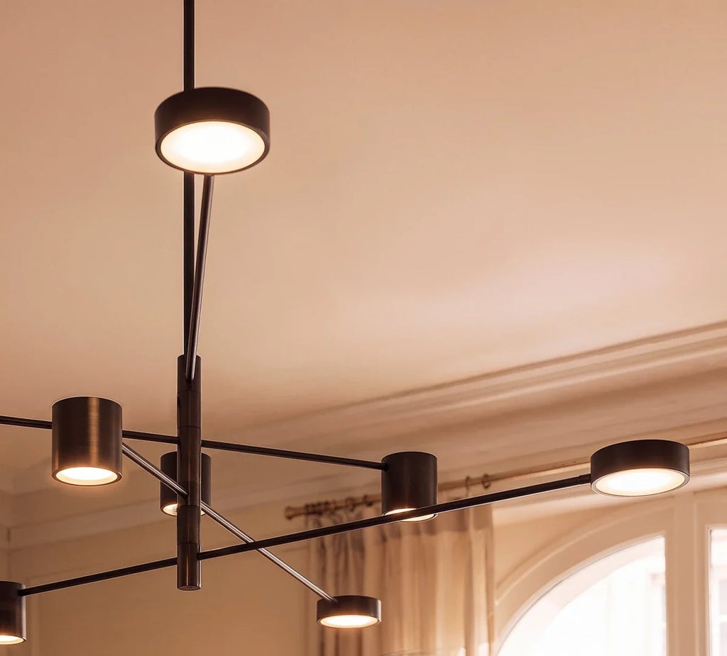 Close view of a Clérachic black chandelier showing its slim arms, dark bronze-toned cylindrical heads and softly glowing round diffusers.