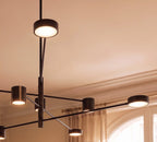 Close view of a Clérachic black chandelier showing its slim arms, dark bronze-toned cylindrical heads and softly glowing round diffusers.