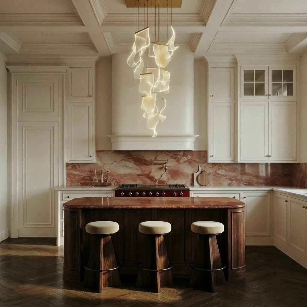 Clérachic column of glowing translucent panels hanging below a gold canopy in a cream panelled kitchen with a marble splashback.