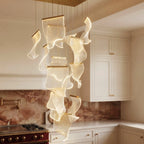 Clérachic chandelier panels lit from within, their curled edges glowing, hung over a cream kitchen with brass-handled cabinets.
