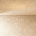 Clérachic flowing gold linear chandelier with a lit LED outline, hung on three fine cables against a textured plaster ceiling.