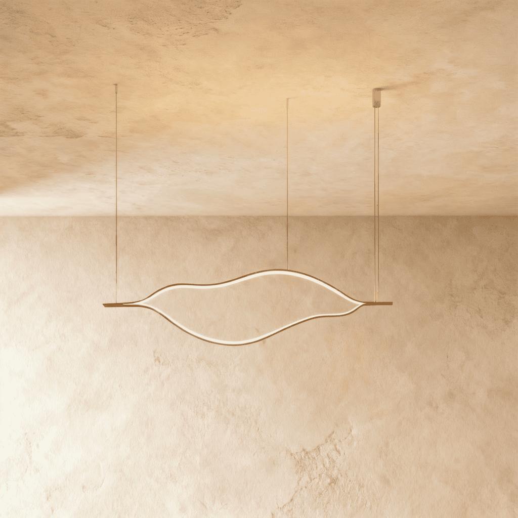Clérachic gold leaf-shaped linear chandelier switched on, suspended from slim cables in front of a softly textured limewashed wall.