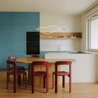 Clérachic gold linear chandelier hanging over a pale oak dining table with red chairs, in a kitchen with teal cabinetry.