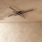 Clérachic black four-bar ceiling light switched off, slim crossed aluminium bars with frosted diffusers on a limewash ceiling.