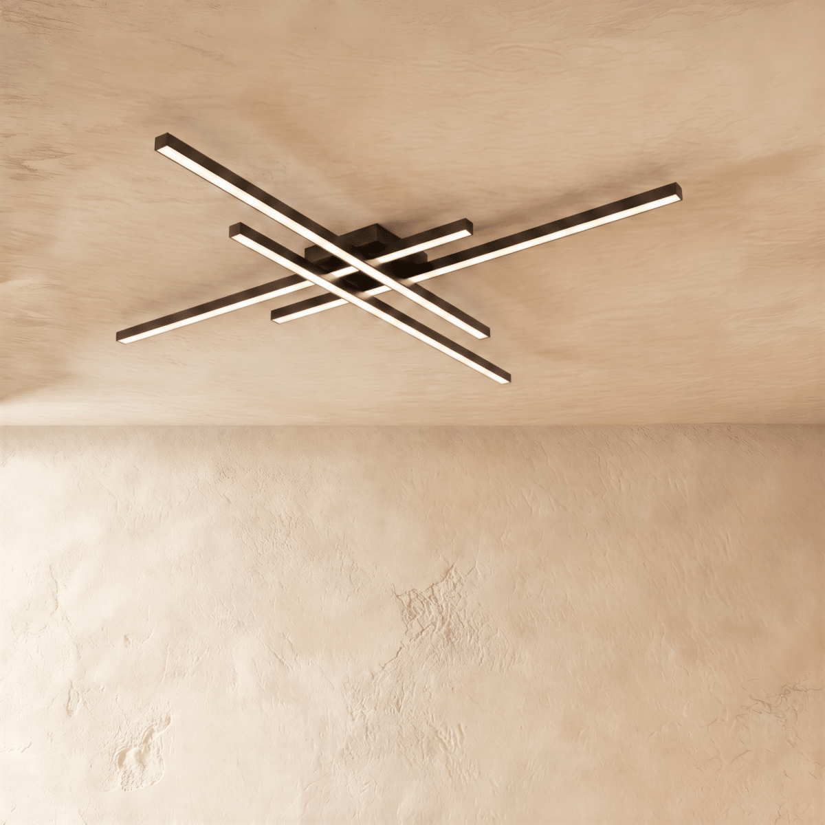 Clérachic larger black ceiling light of four crossed LED bars, lit warm and spanning a wide stretch of limewash ceiling.