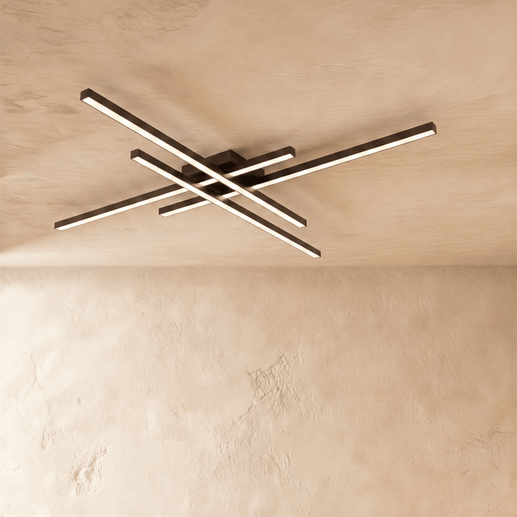 Clérachic black four-bar LED ceiling light lit warm, the crossed aluminium bars reaching wide across a limewash ceiling.