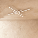 Clérachic white ceiling light of four crossed LED bars, slim aluminium arms glowing soft white on a limewash ceiling.