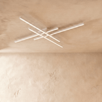 Clérachic white four-bar LED ceiling light in a larger size, thin crossed aluminium arms lit softly on limewash.