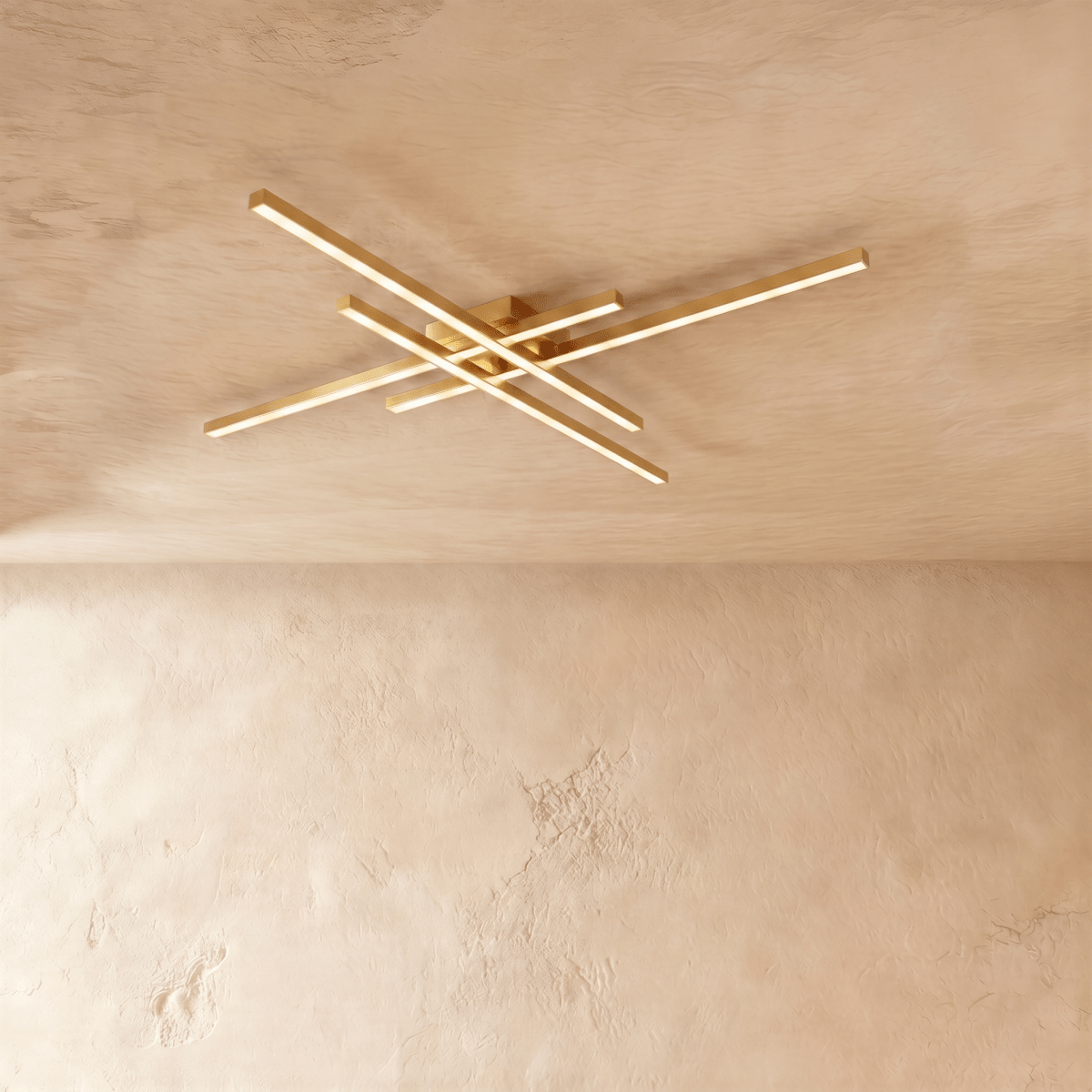 Clérachic gold four-bar LED ceiling light, slim brushed brass crossed arms glowing warm on a limewash ceiling.