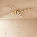 Clérachic gold crossed-bar LED ceiling light in a larger size, four brass-toned bars lit warm on limewash.