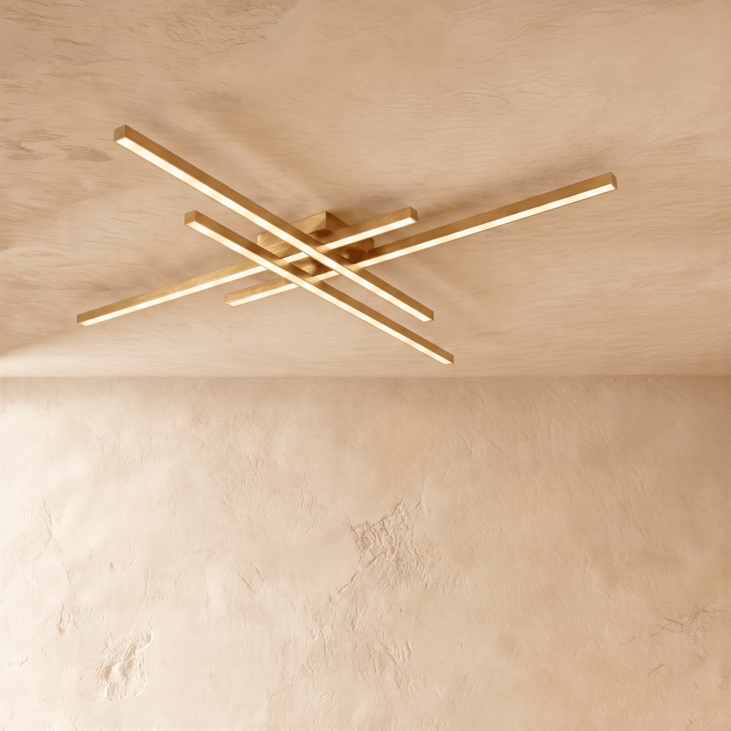 Clérachic gold four-bar LED ceiling light in a long size, brass-toned crossed arms spanning a limewash ceiling.