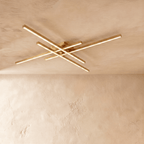 Clérachic gold four-bar LED ceiling light in a long size, brass-toned crossed arms spanning a limewash ceiling.