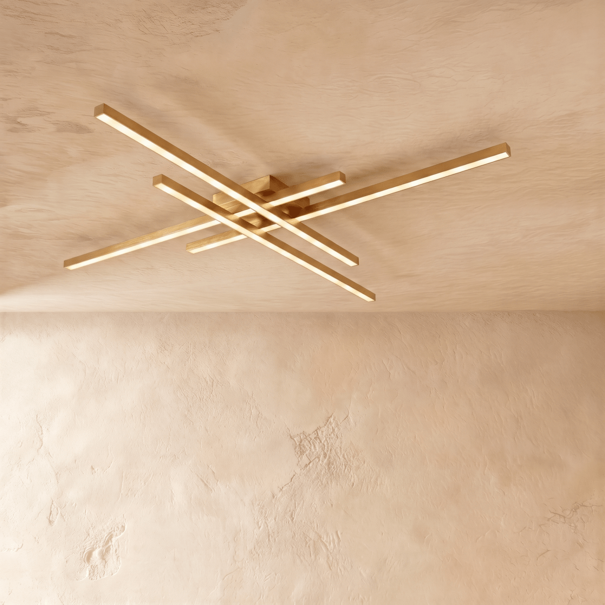 Clérachic gold four-bar LED ceiling light in a long size, brass-toned crossed arms spanning a limewash ceiling.
