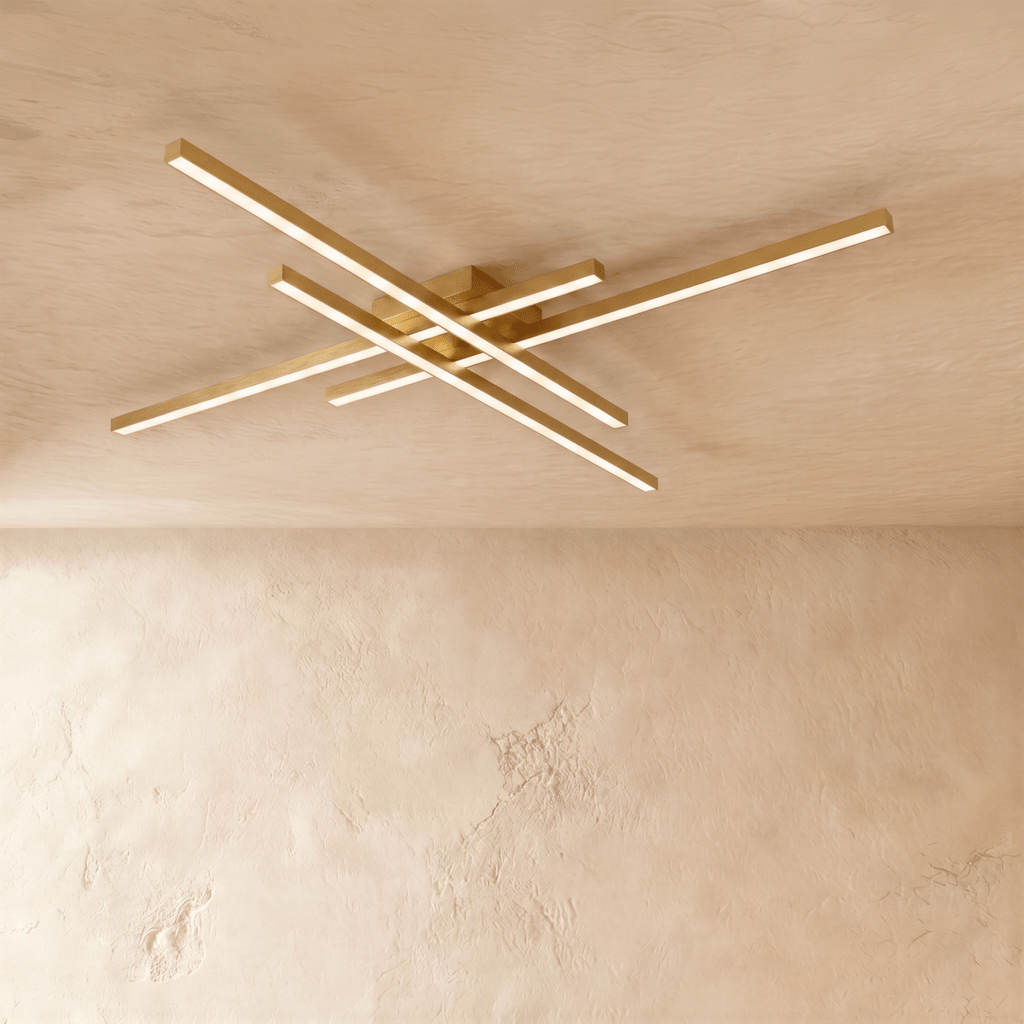 Clérachic gold four-bar LED ceiling light at its widest, thin brass-toned crossed bars lit warm on limewash.