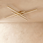 Clérachic gold four-bar LED ceiling light at its widest, thin brass-toned crossed bars lit warm on limewash.