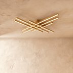 Clérachic gold six-bar LED ceiling light, two tiers of crossed brass-toned bars glowing warm on a limewash ceiling.