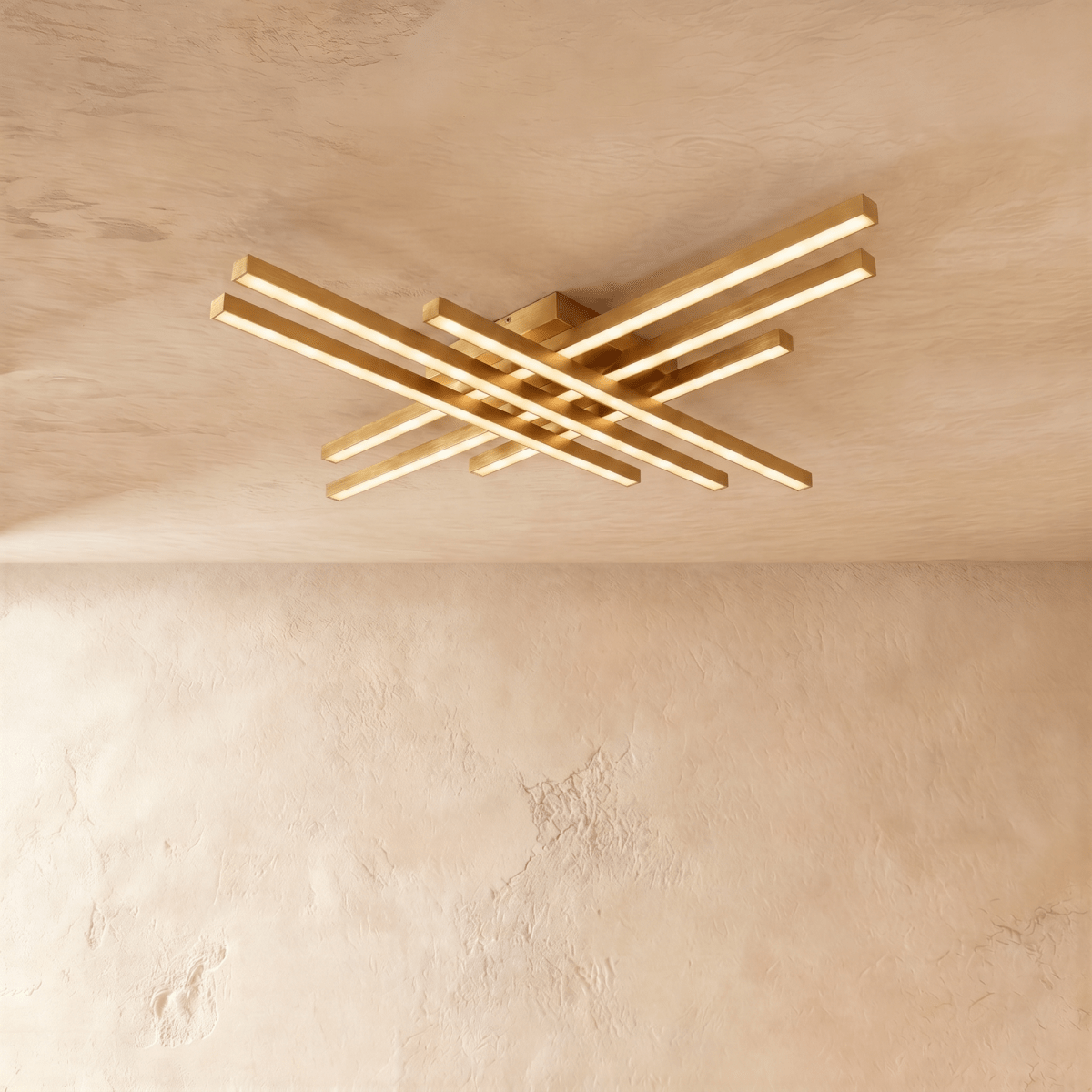 Clérachic gold six-bar LED ceiling light, two tiers of crossed brass-toned bars glowing warm on a limewash ceiling.