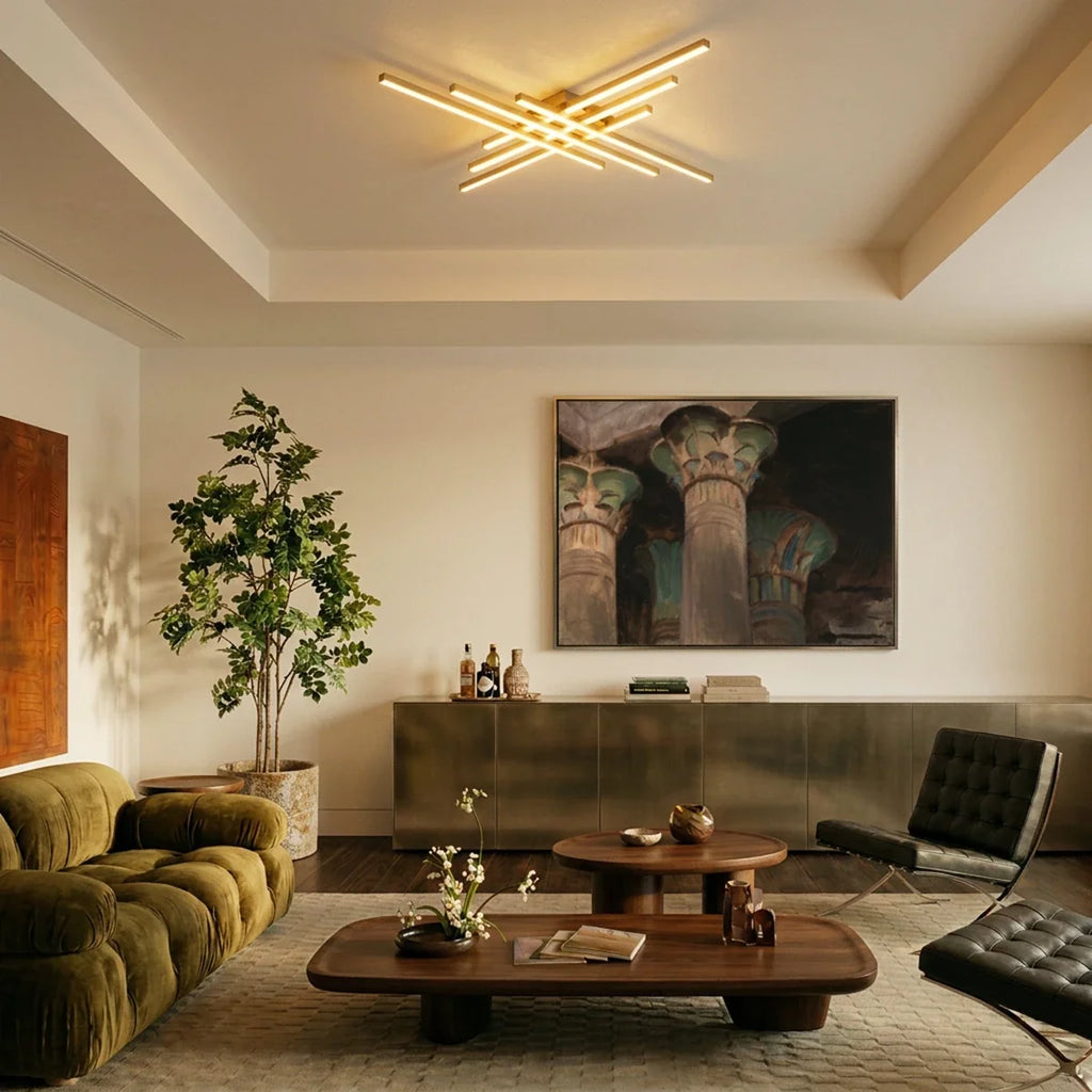 Clérachic gold six-bar LED ceiling light over a living room with an olive velvet sofa, walnut tables and a framed painting.