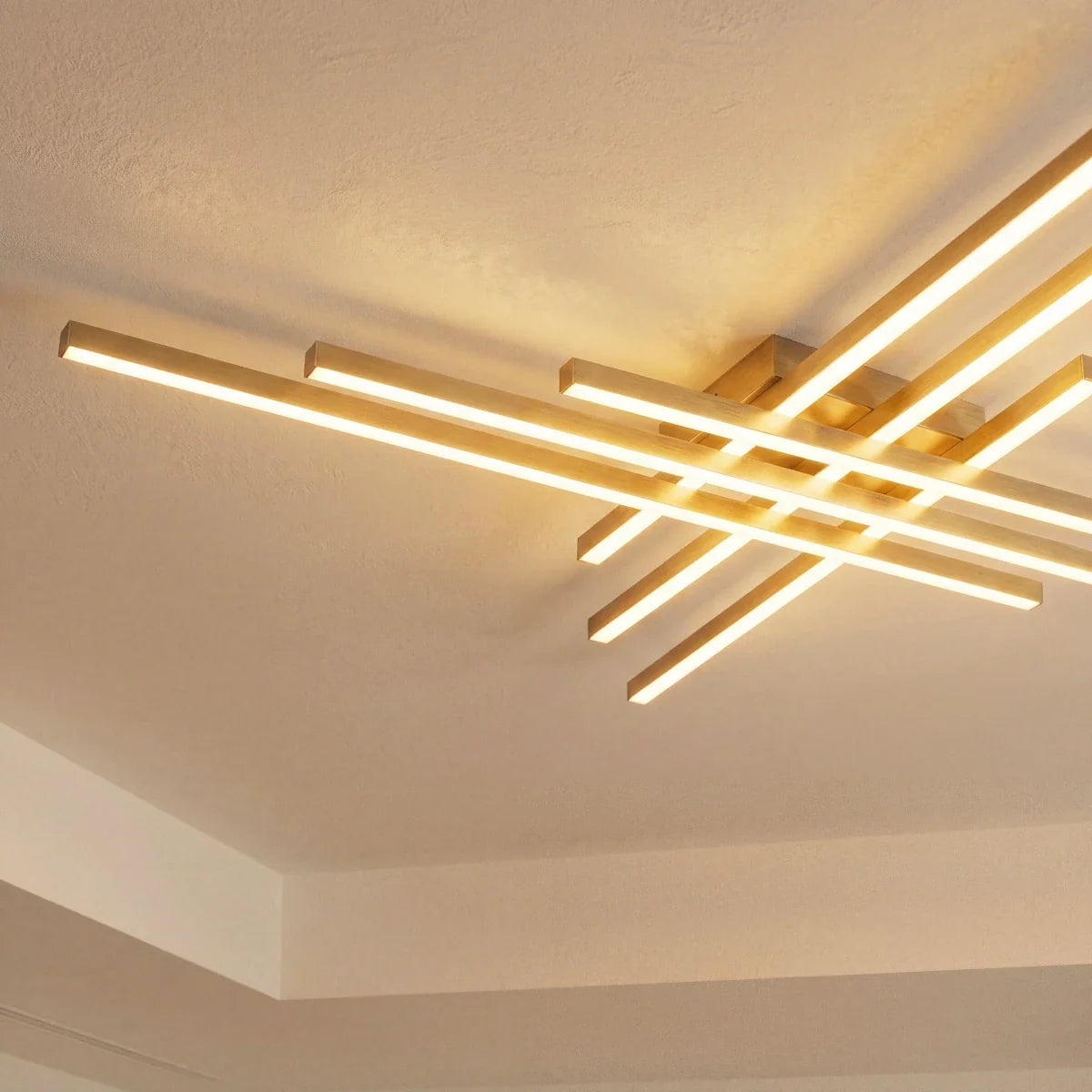 Clérachic gold six-bar LED ceiling light close up, warm frosted bars crossing in two layers on a plain white ceiling.
