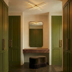 Clérachic gold crossed-bar LED ceiling light in a dressing area with olive wardrobes, a mirror and a velvet stool.