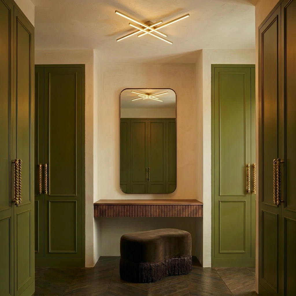 Clérachic gold crossed-bar LED ceiling light in a dressing area with olive wardrobes, a mirror and a velvet stool.