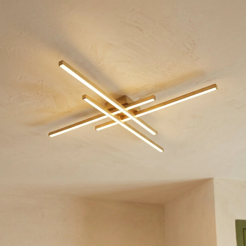 Clérachic gold four-bar LED ceiling light from below, brushed brass bars with soft frosted light on a limewash ceiling.