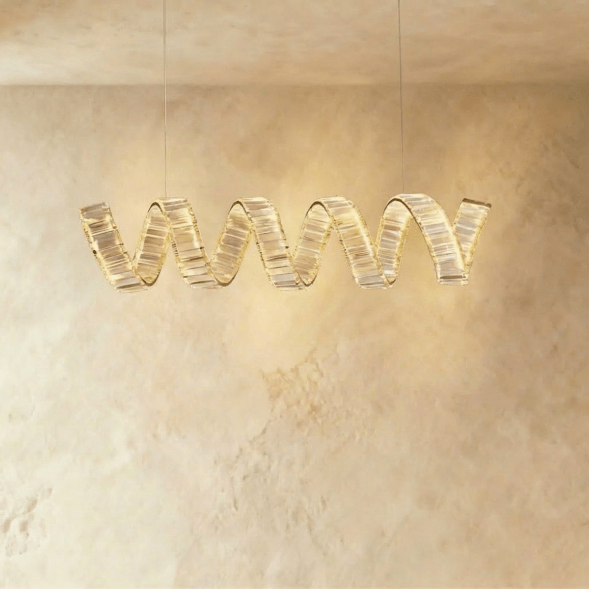 Clérachic single-wave spiral chandelier in gold, with a ribbon of clear crystal blocks glowing warmly on two cables.