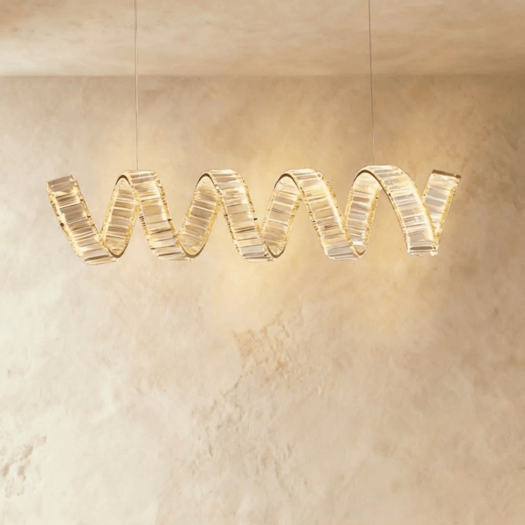 Clérachic longer single-wave spiral chandelier in gold, crystal blocks lit from within against a limewashed wall.