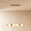 Clérachic linear pendant of four alabaster cylinders joined by brass bands, lit warm on two cords in a studio room.