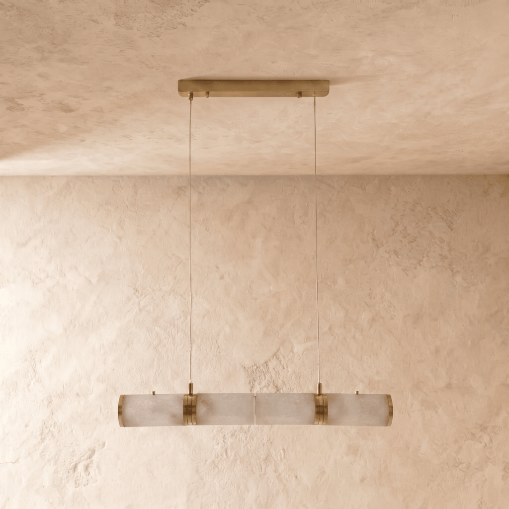 Clérachic linear pendant of four alabaster cylinders with brass bands, switched off, hung on two cords against limewash.