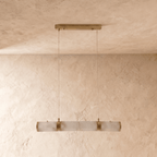 Clérachic linear pendant of four alabaster cylinders with brass bands, switched off, hung on two cords against limewash.
