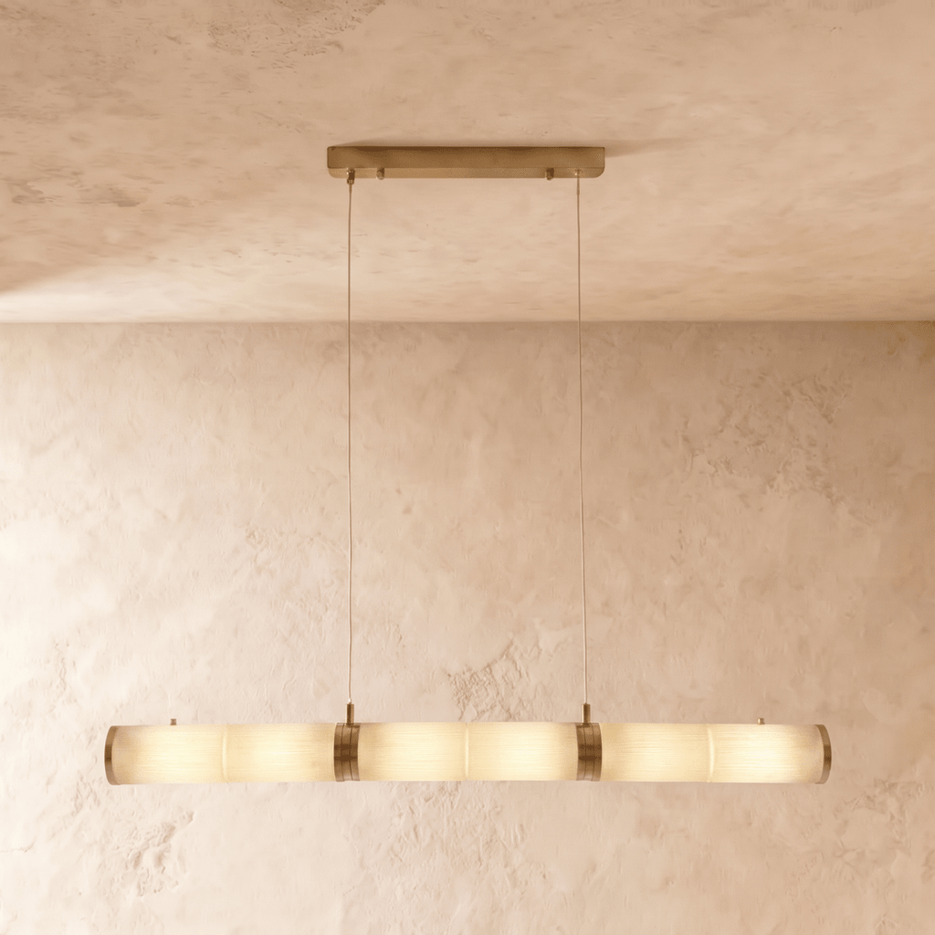 Clérachic longer linear pendant of alabaster cylinders and brass bands, glowing softly on two cords in a studio room.