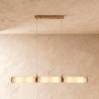Clérachic longer linear pendant of alabaster cylinders and brass bands, glowing softly on two cords in a studio room.