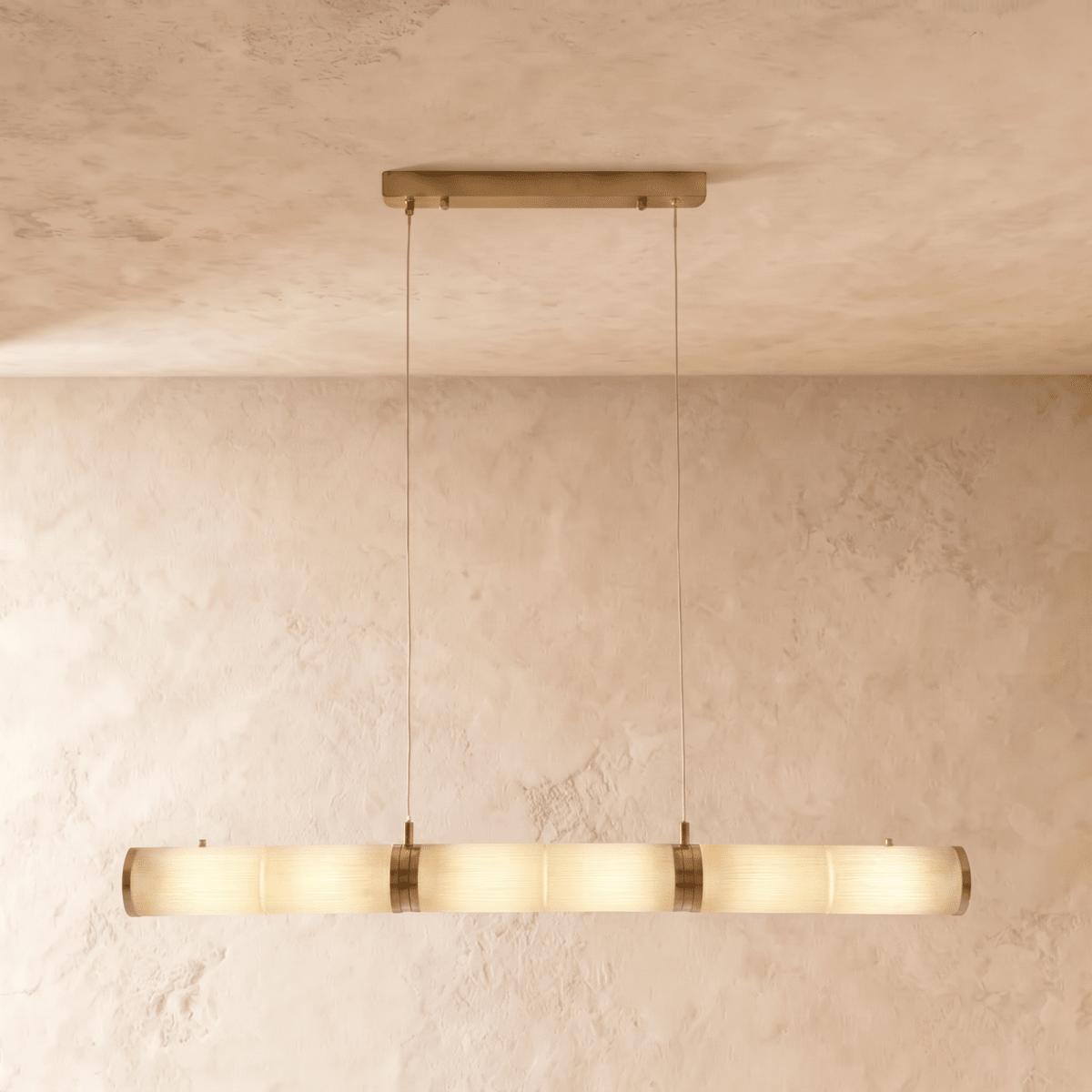 Clérachic longer linear pendant of alabaster cylinders and brass bands, glowing softly on two cords in a studio room.