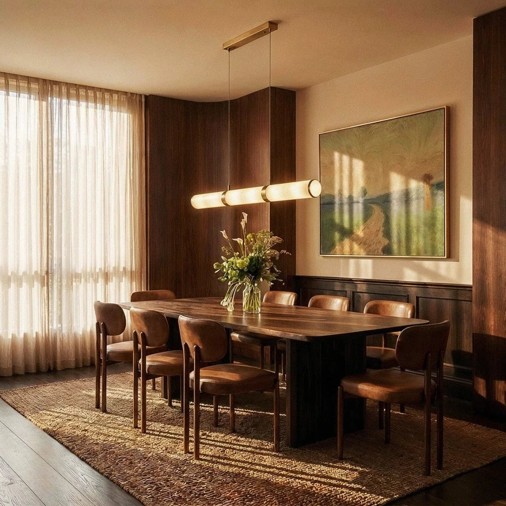 Clérachic alabaster linear pendant hung over a long walnut dining table in a warm room with tall sheer curtains.