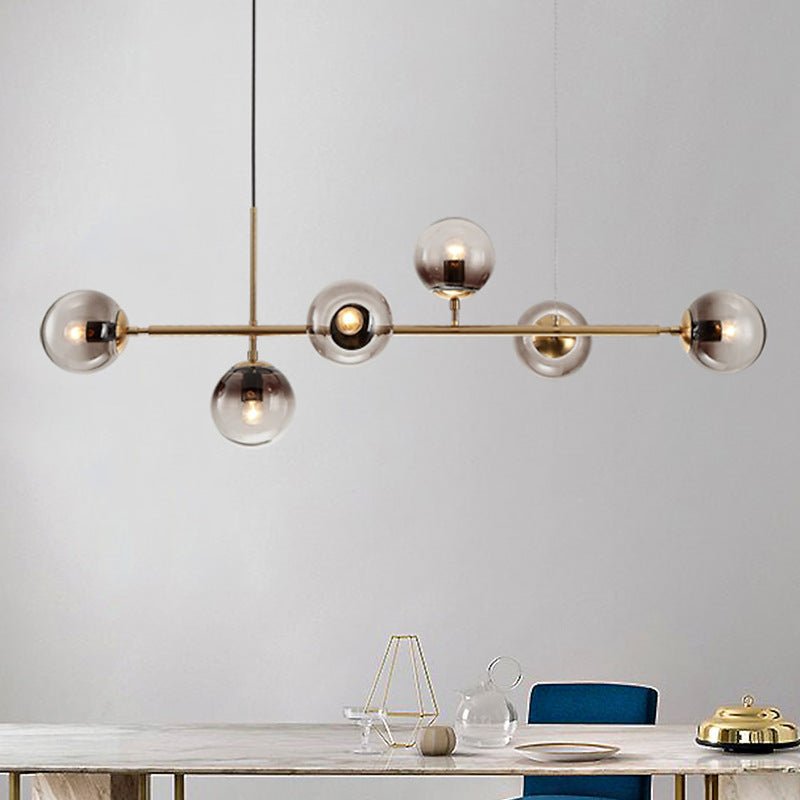Close view of this Clérachic pendant's brass bar and six graduated smoke-grey globes, hanging over a marble-topped table.