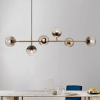Close view of this Clérachic pendant's brass bar and six graduated smoke-grey globes, hanging over a marble-topped table.