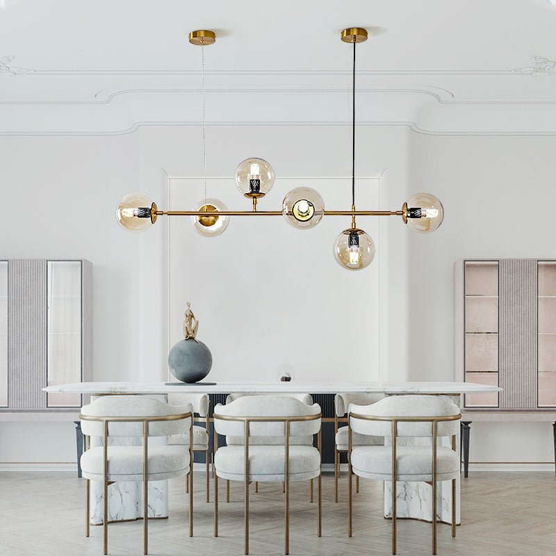A Clérachic pendant of six amber-toned orbs hangs low in a bright, moulded-ceiling dining room with cream upholstered chairs.