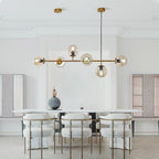 A Clérachic pendant of six amber-toned orbs hangs low in a bright, moulded-ceiling dining room with cream upholstered chairs.