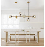 Over a pale wood dining table in a light kitchen, the brass rod and six clear amber orbs of this Clérachic pendant glow softly.