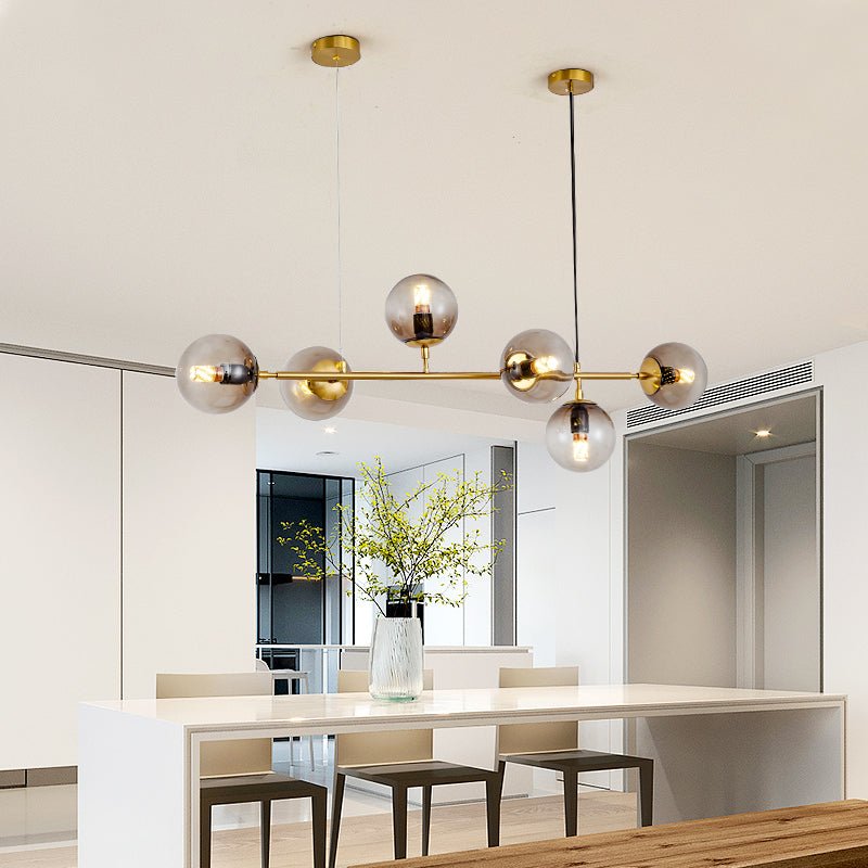Seen against a cream ceiling, this Clérachic pendant sets six smoke-tinted orbs along a brass bar above a white island counter.